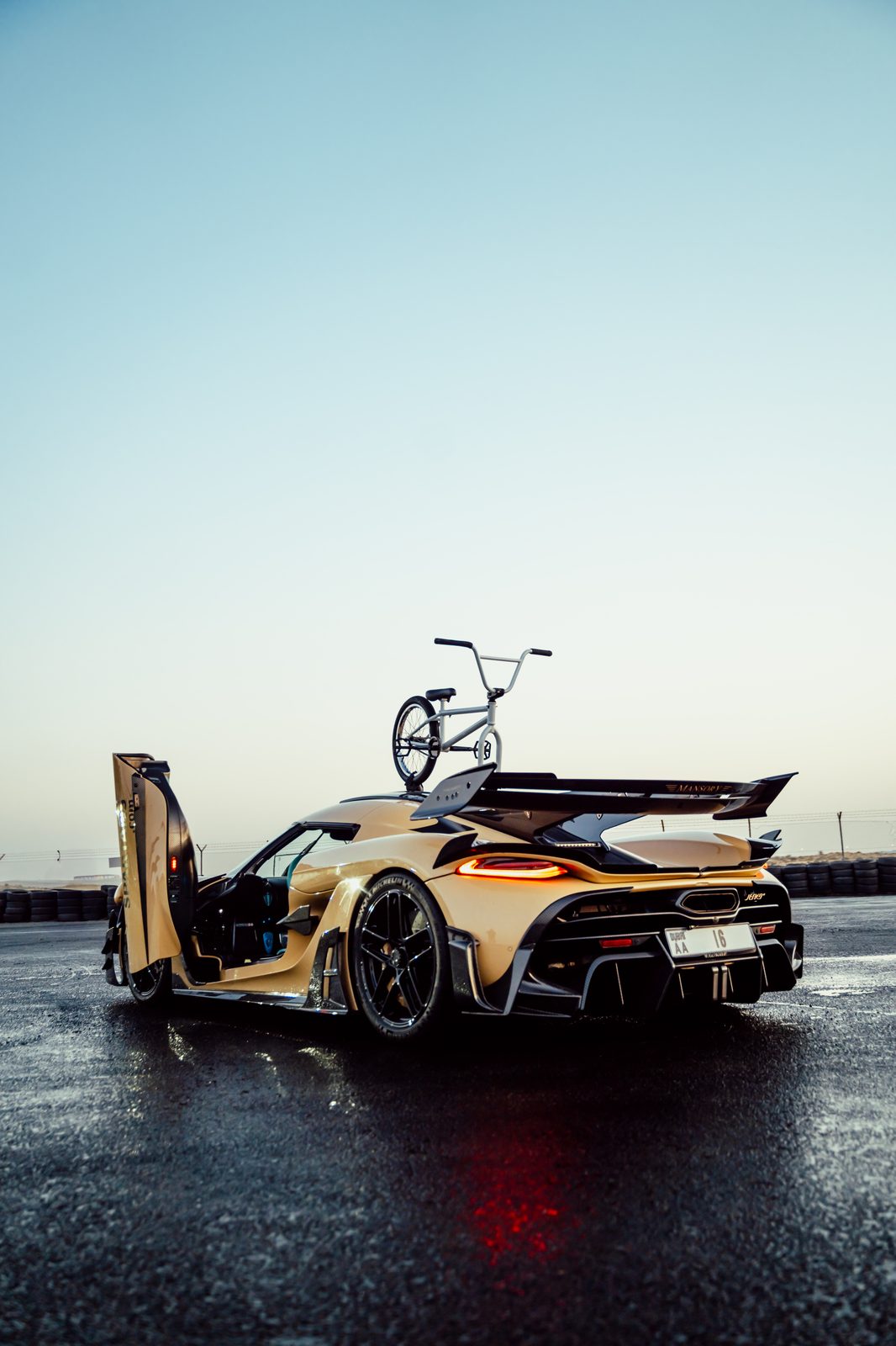 Koenigsegg Jesko with a BMX resting on the rear wing, wet track at dawn
