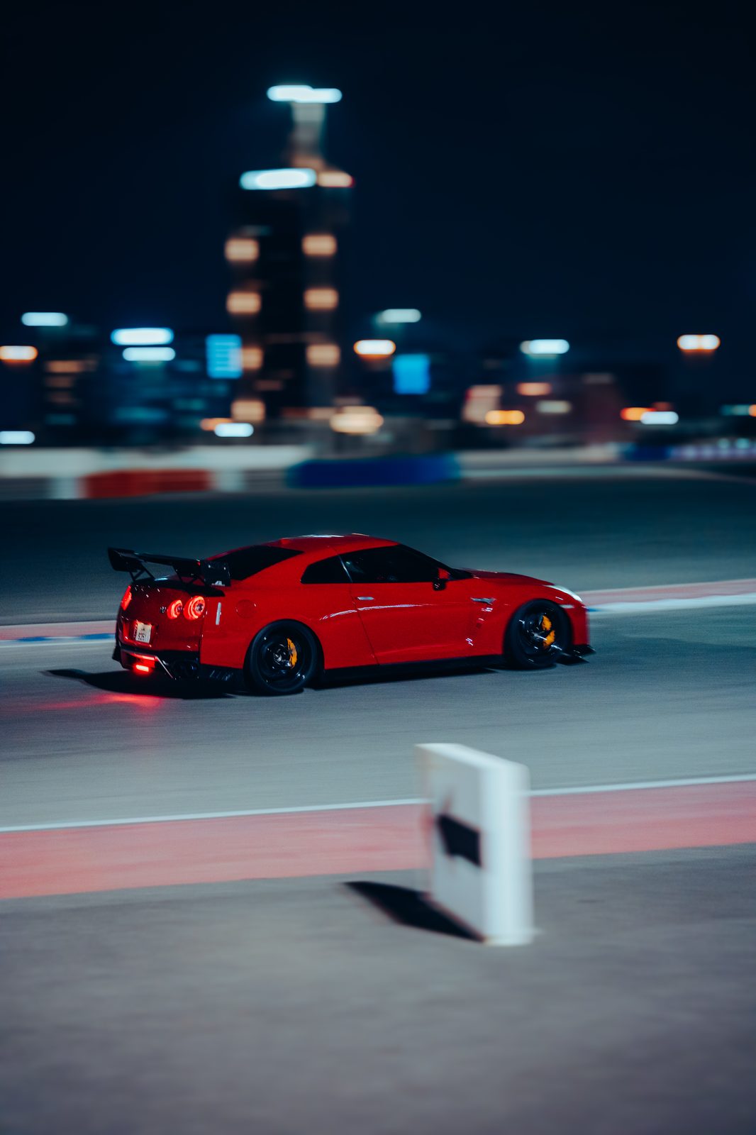 Red Nissan GT-R R35 with a rear wing, panning shot on track at night