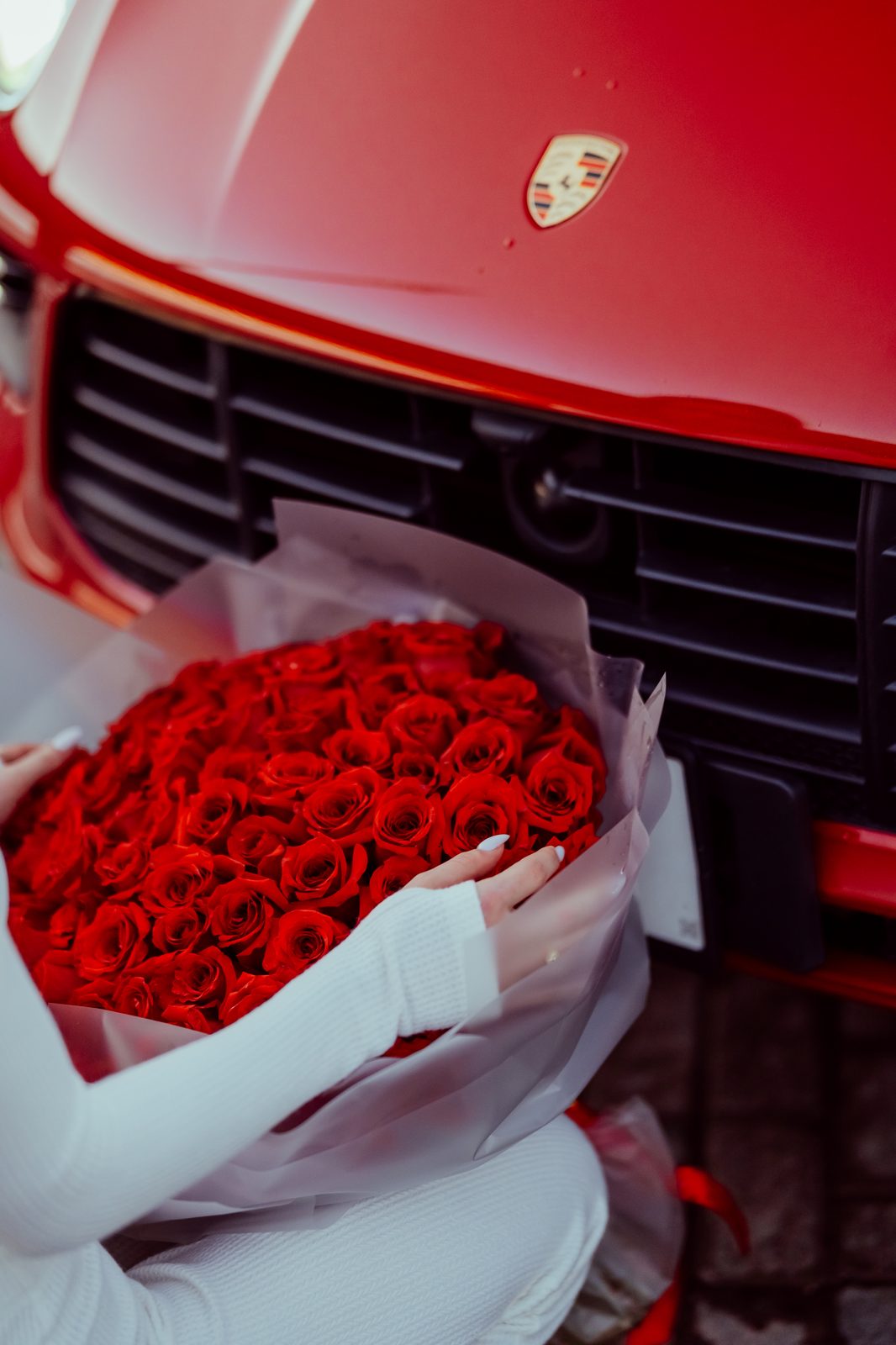 A hundred red roses presented at the nose of a red Porsche